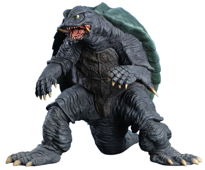 A detailed monster figurine of a reptilian kaiju with a dark gray textured body, green shell, and open mouth showing sharp teeth, isolated on a white background.