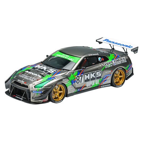 A scale model of a Nissan GT-R Nismo race car with a silver, green, and blue livery, featuring gold wheels and various sponsor decals including HKS, Panasonic, and Yokohama.