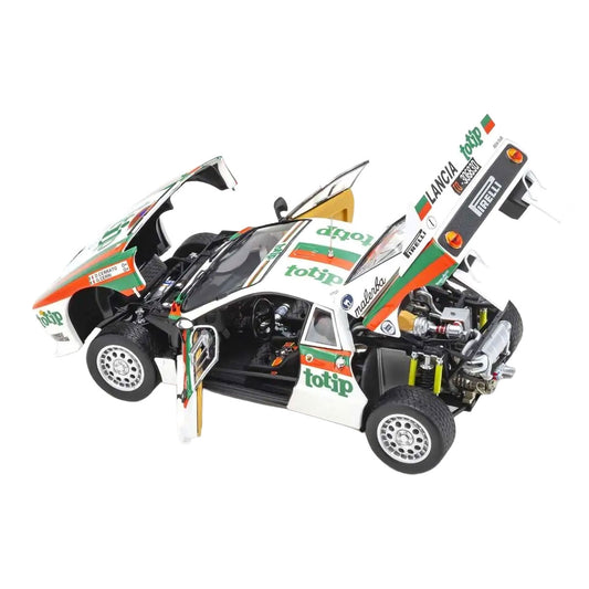 A detailed model of a Lancia rally car with its doors and hood open, showcasing the interior and engine. The car is primarily white with green and orange sponsor decals, including Totip and Pirelli.